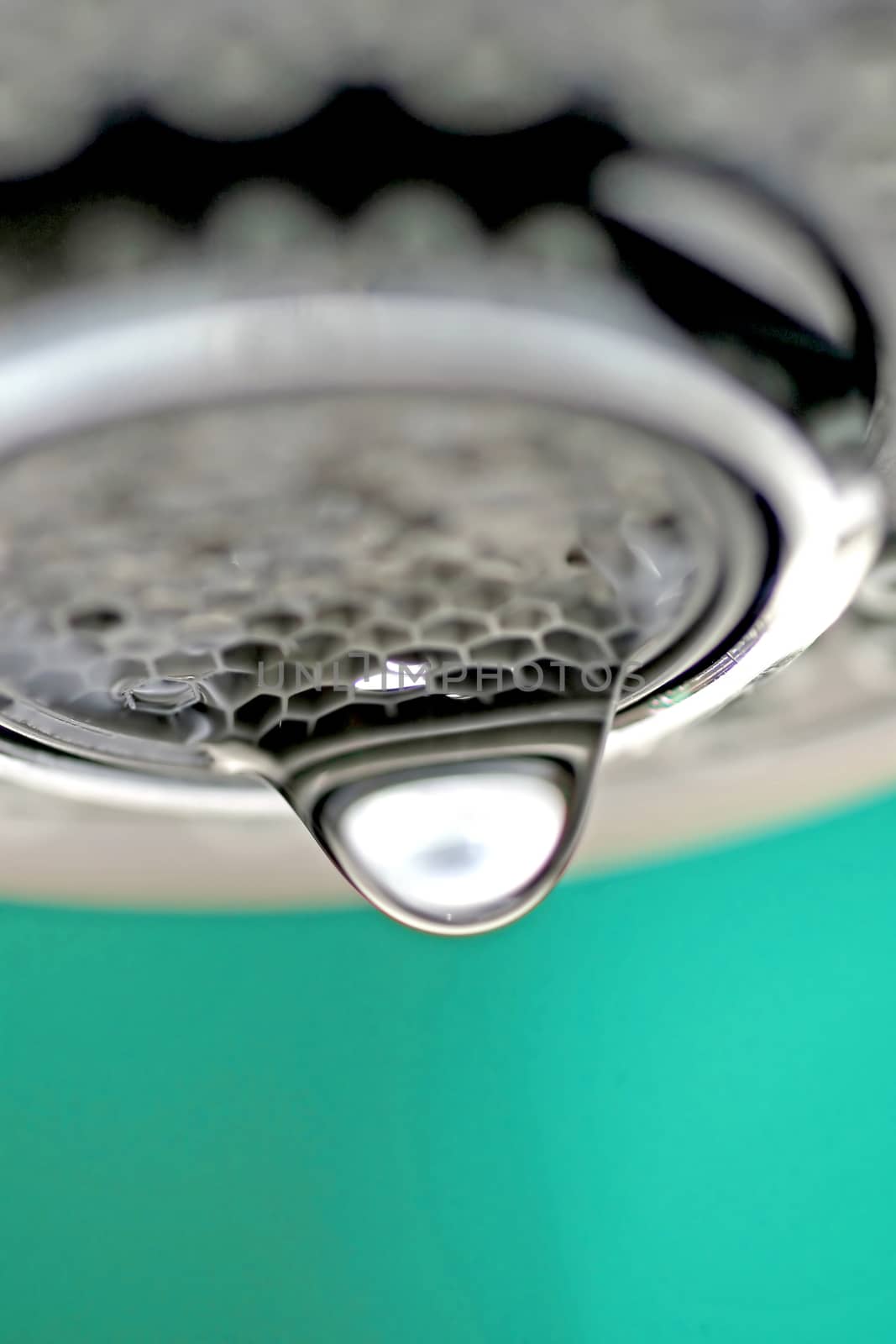 A macro of a white tap / faucet dripping with blue background.