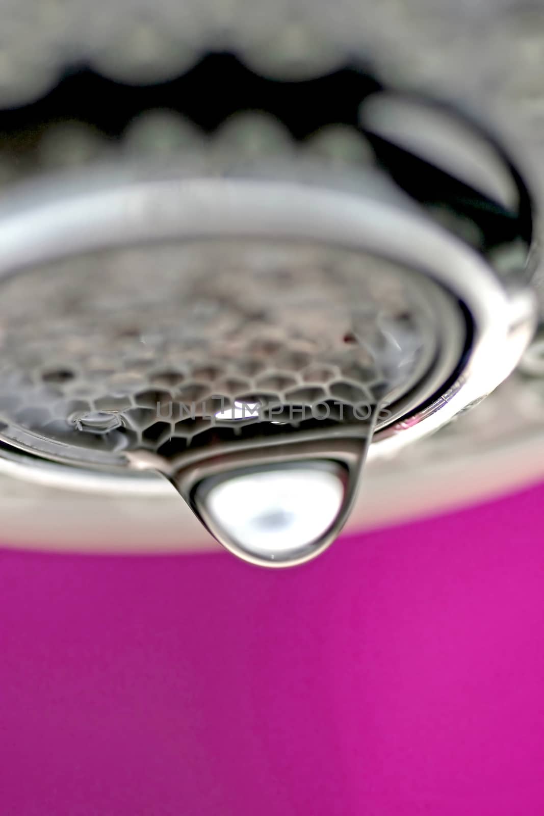 A macro of a white tap / faucet dripping with pink background.