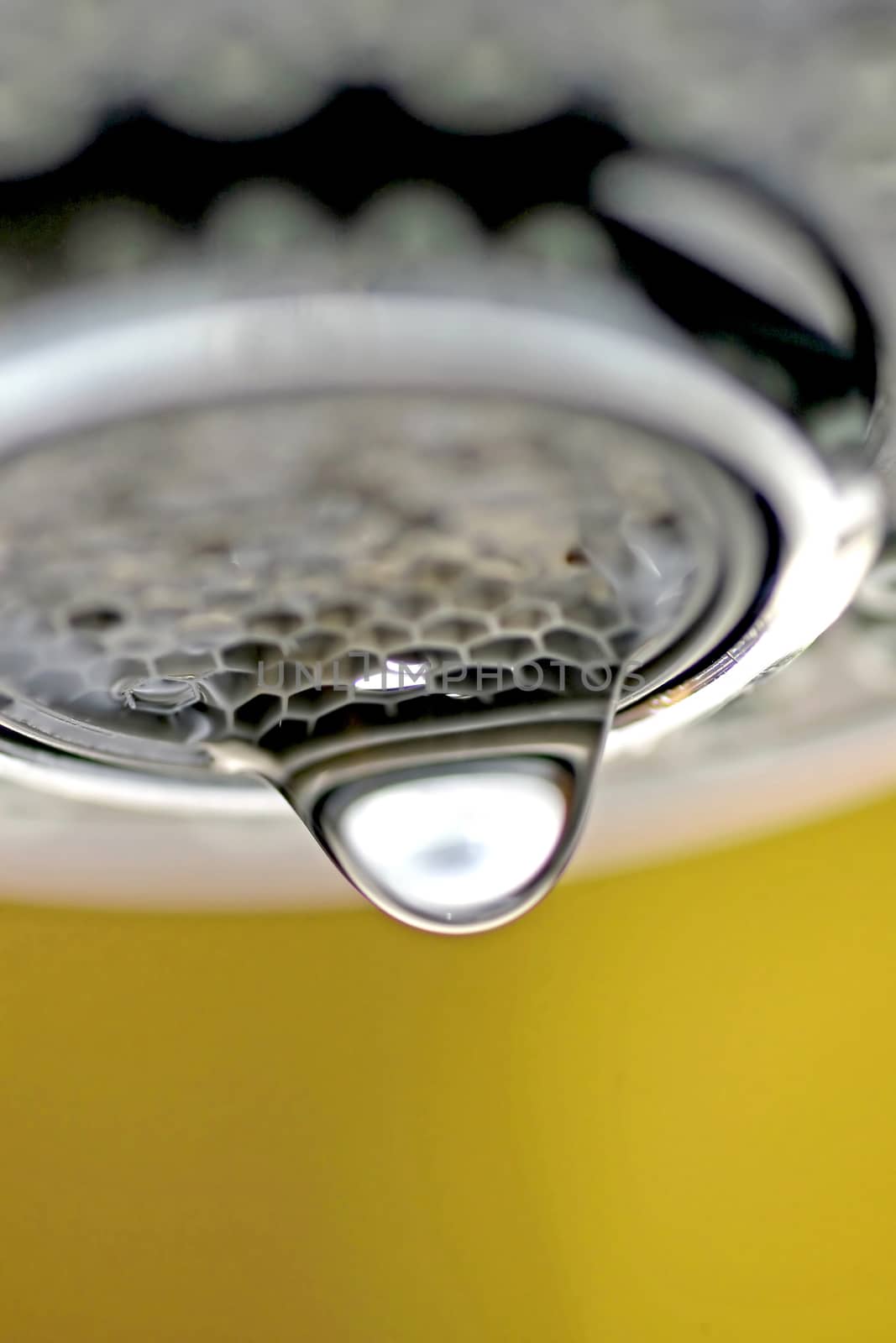 A macro of a white tap / faucet dripping with yellow background.