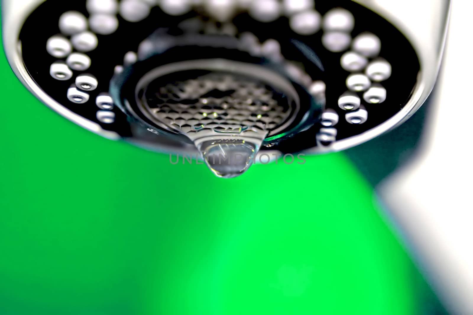 A macro of a white tap / faucet dripping with green background.