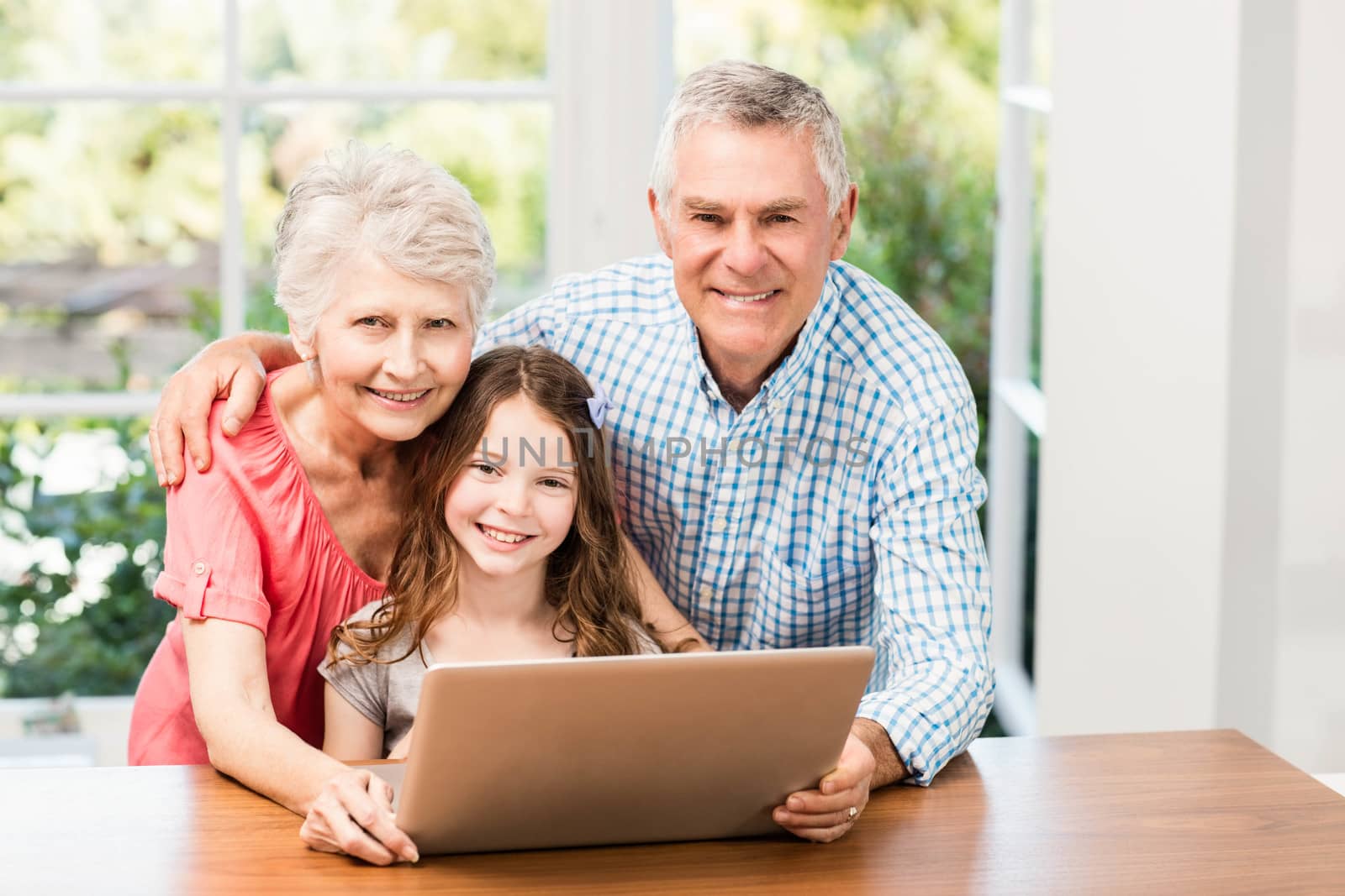 Portrait of smiling grandparents and granddaughter using laptop at home