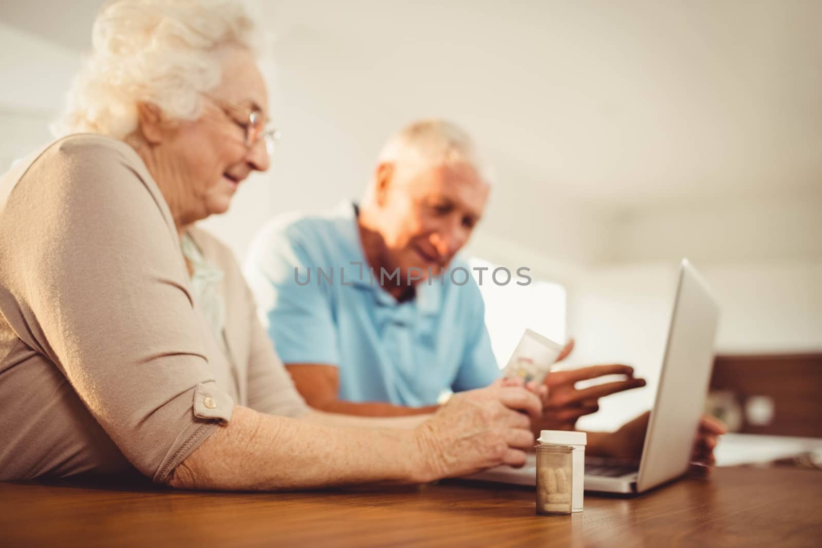 Senior couple using laptop and holding pills by Wavebreakmedia