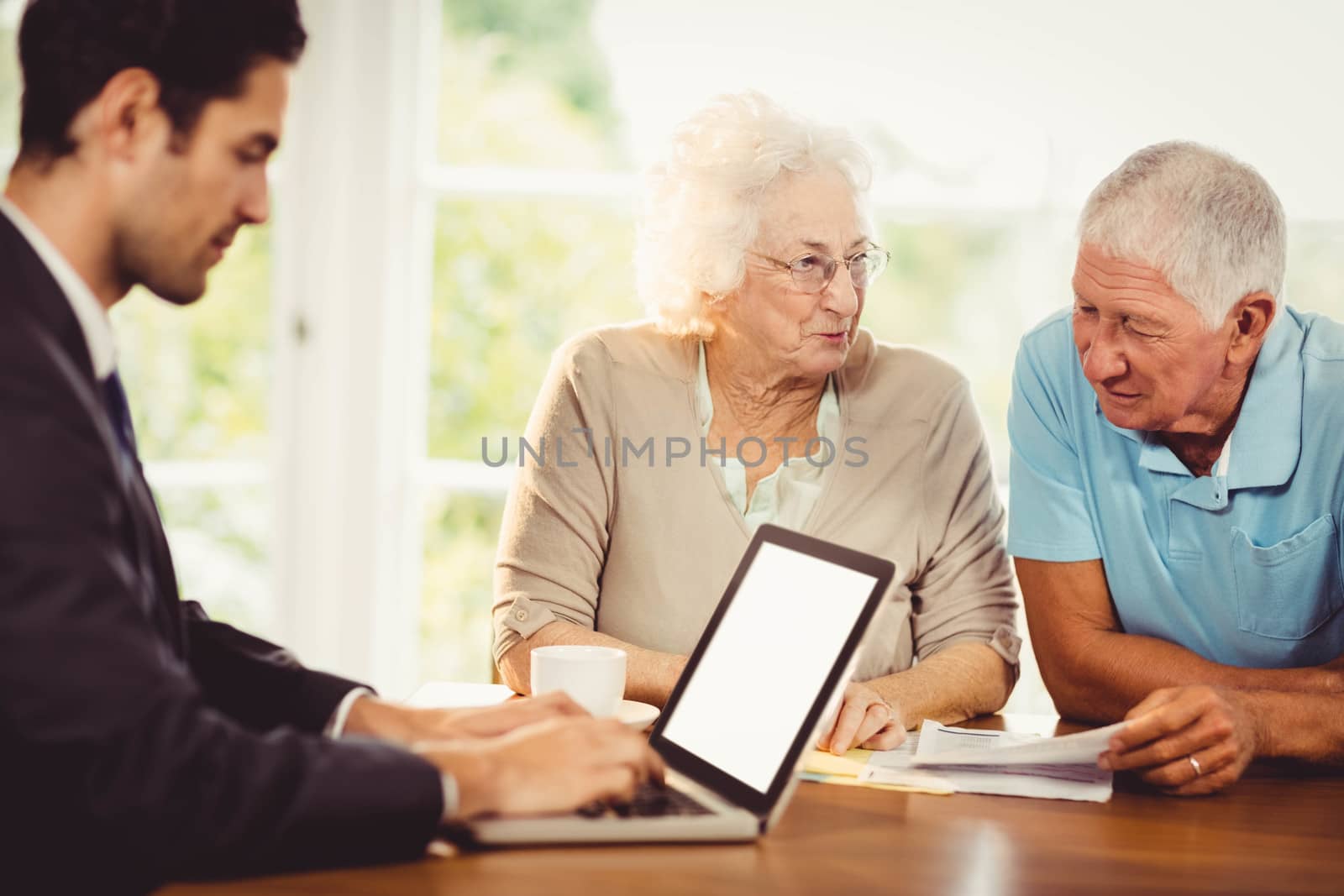 Businessman using laptop while senior couple is reading documents at home