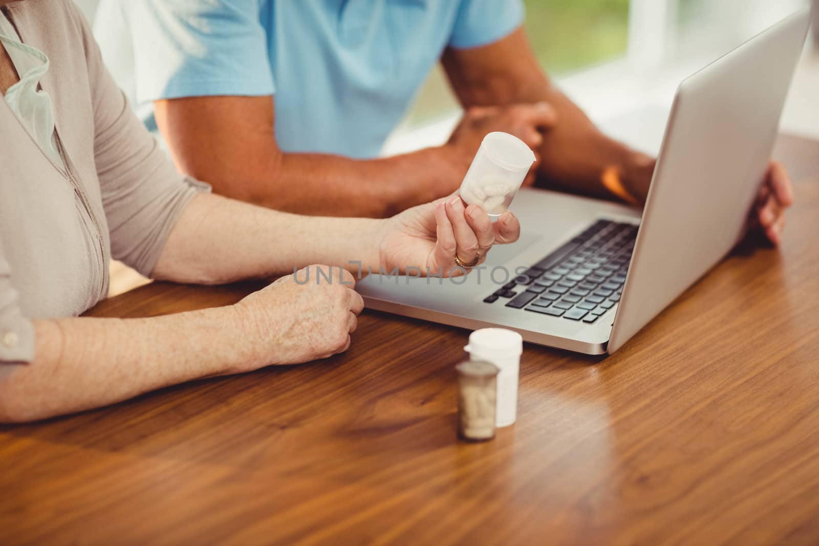 Senior couple using laptop and holding pills at home