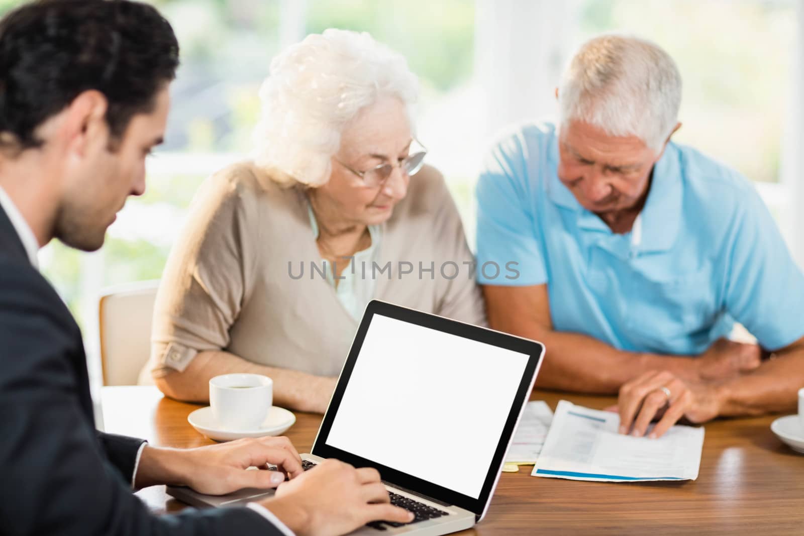 Businessman using laptop while senior couple is reading documents by Wavebreakmedia