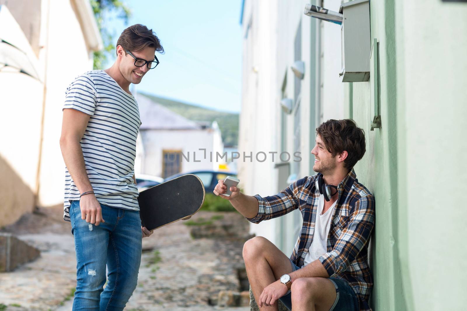 Hip men talking in the city holding skateboard and smartphone