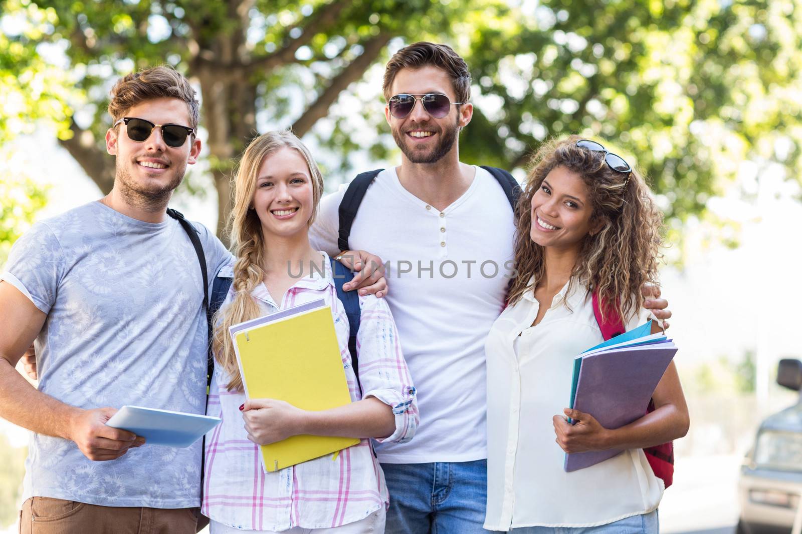 Hip friends holding notebooks and smiling at the camera outdoors