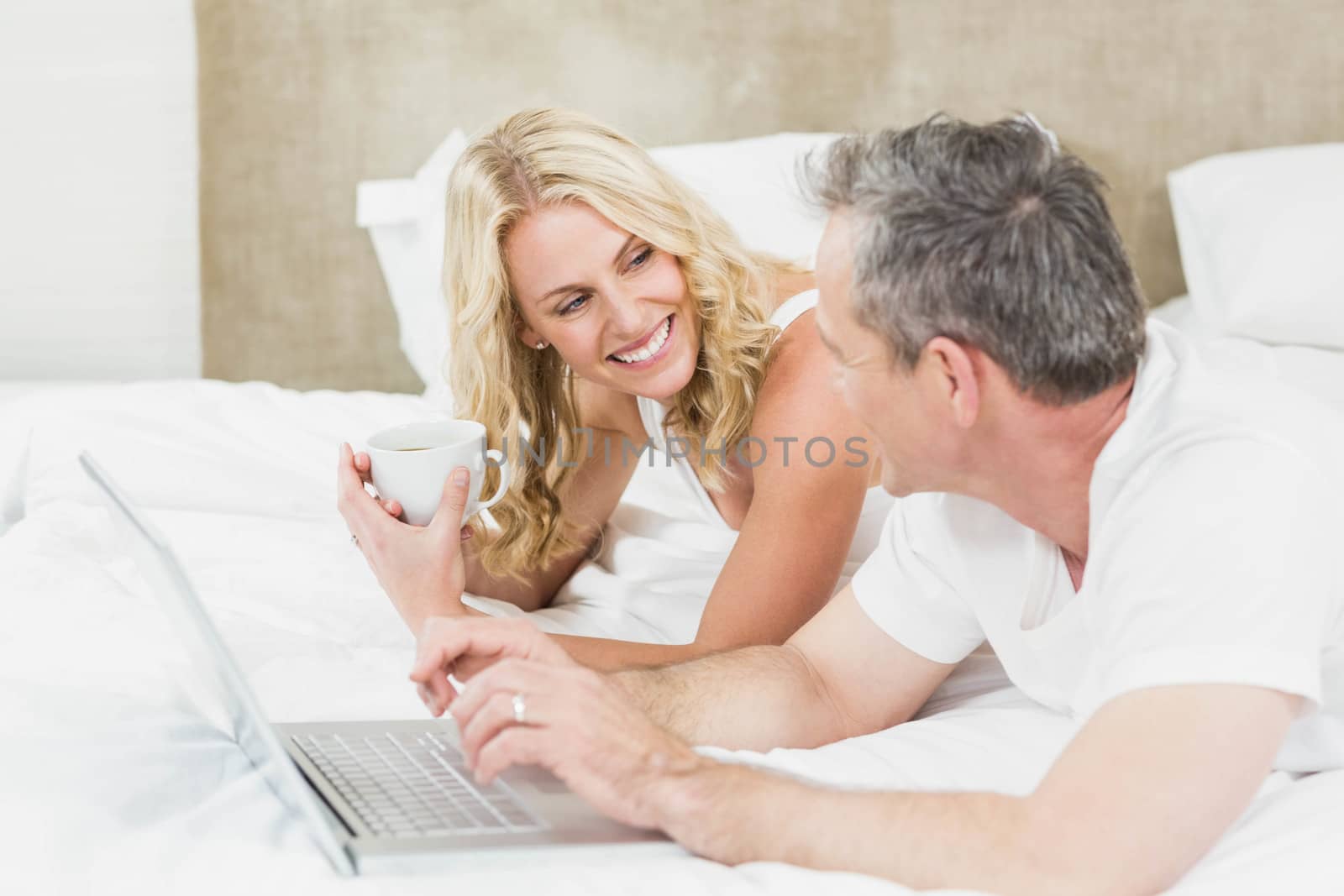 Cute couple using laptop in bed in their bedroom