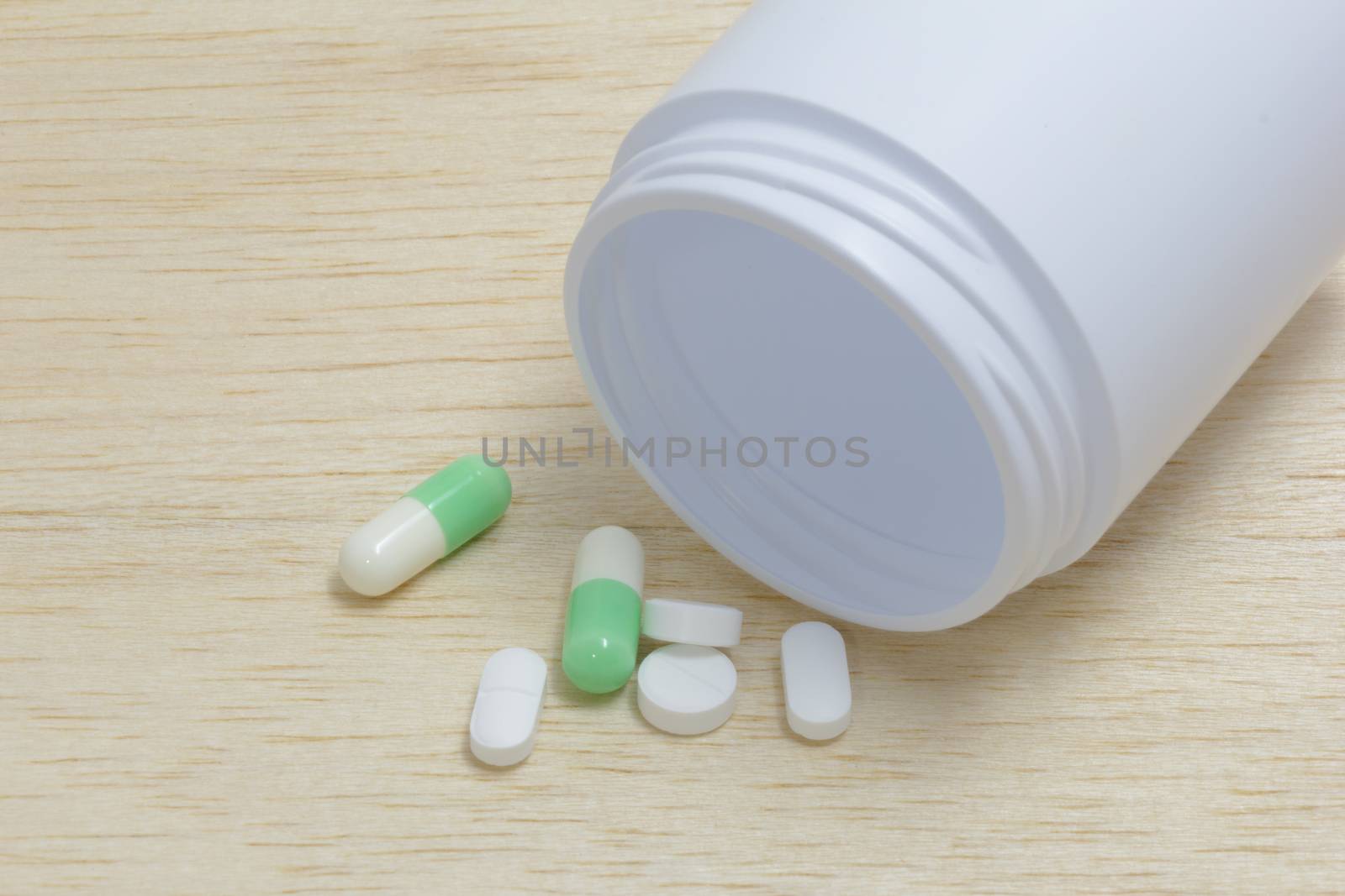 Pills spilling out of pill bottle on wood back ground by chingraph