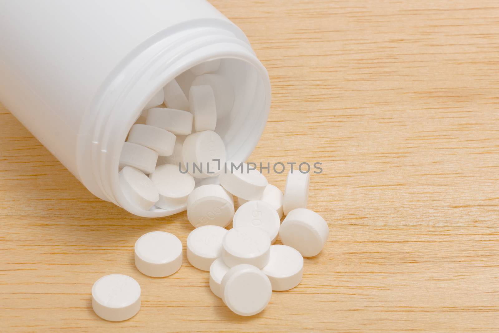 Pills spilling out of pill bottle on wood back ground by chingraph
