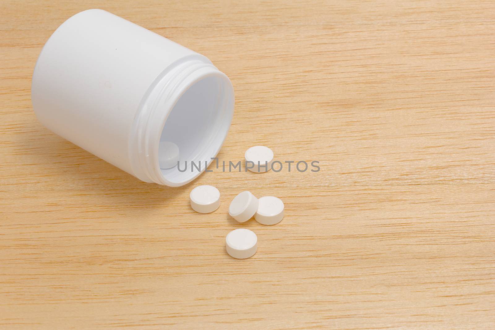 Pills spilling out of pill bottle on wood back ground