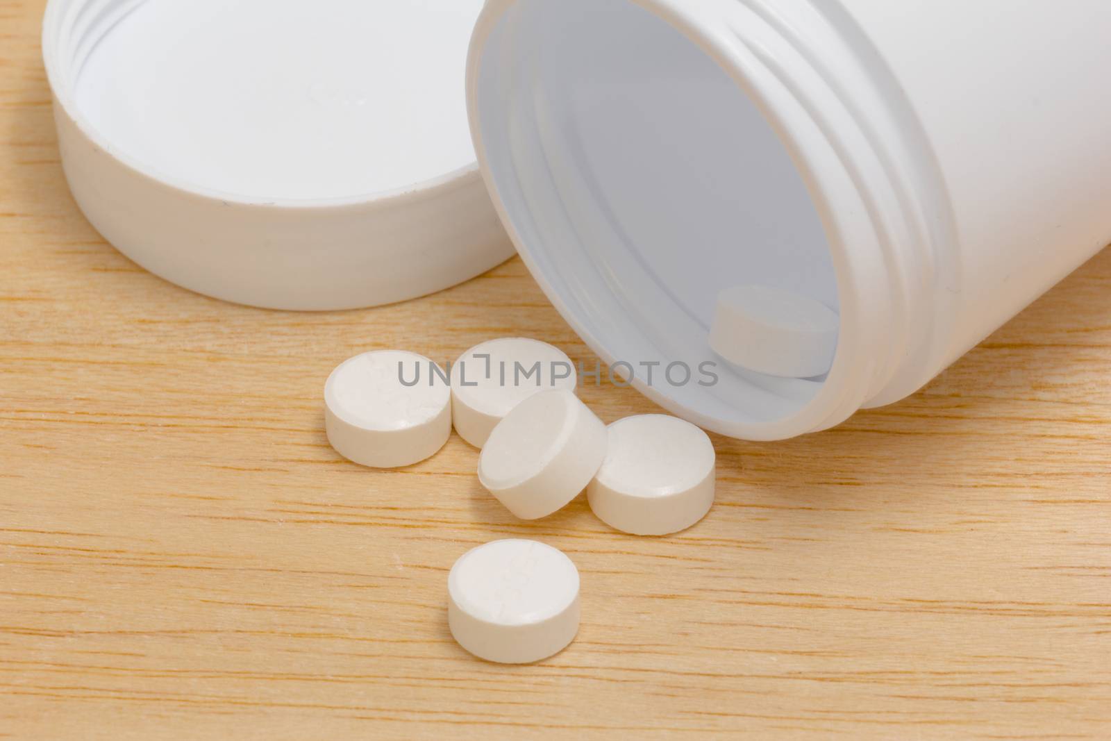Pills spilling out of pill bottle on wood back ground