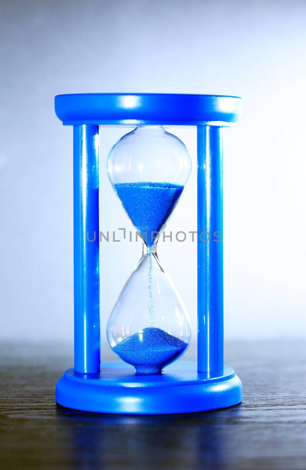 Time concept. Hourglass with blue sand on nice gray background