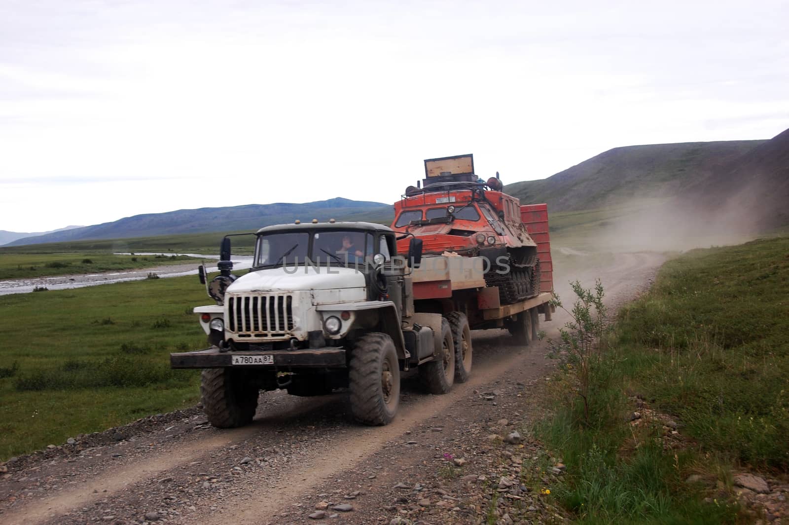 Truck carries all-terrain tracked vehicle at gravel road tundra area, Chukotka, Russia