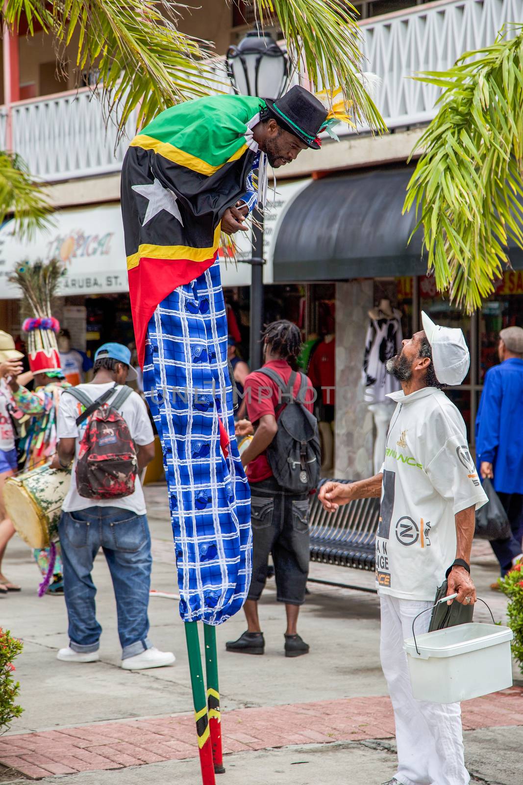 Basseterre, Saint Kitts and Nevis- June 21, 2013: Street performer wrapped up in his nation's flag and standing on stills stops to talk to a man after dancing with his dance troupe at Port Zante