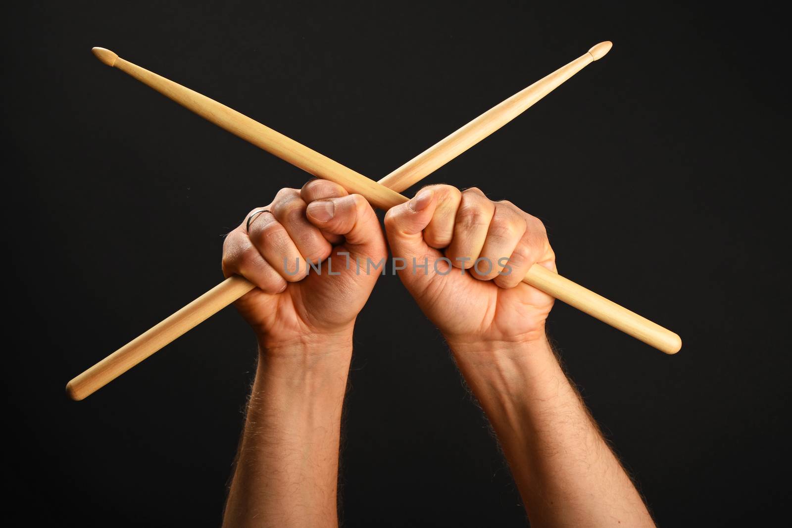 Two man hands holding crossed wooden drumsticks over black background