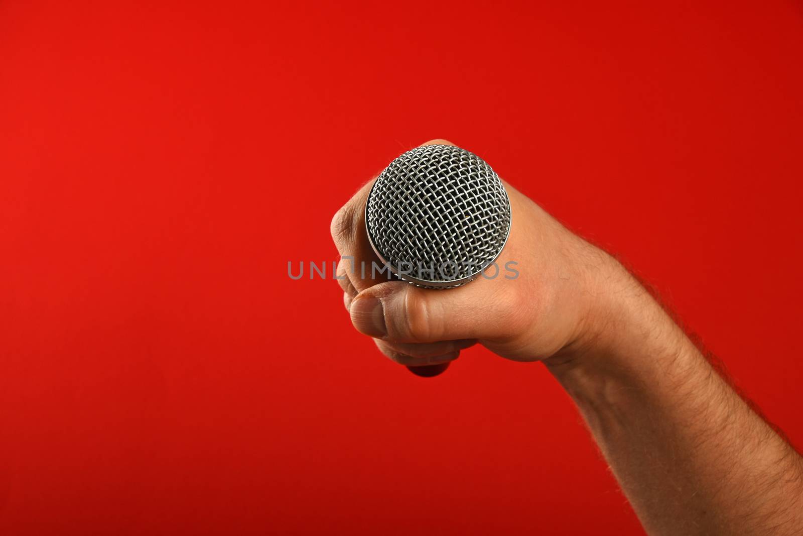 Man hand holding voice microphone in fist over red background
