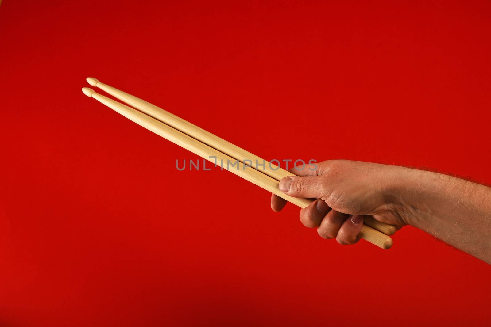Man hand holding two wooden drumsticks over red background, diagonal