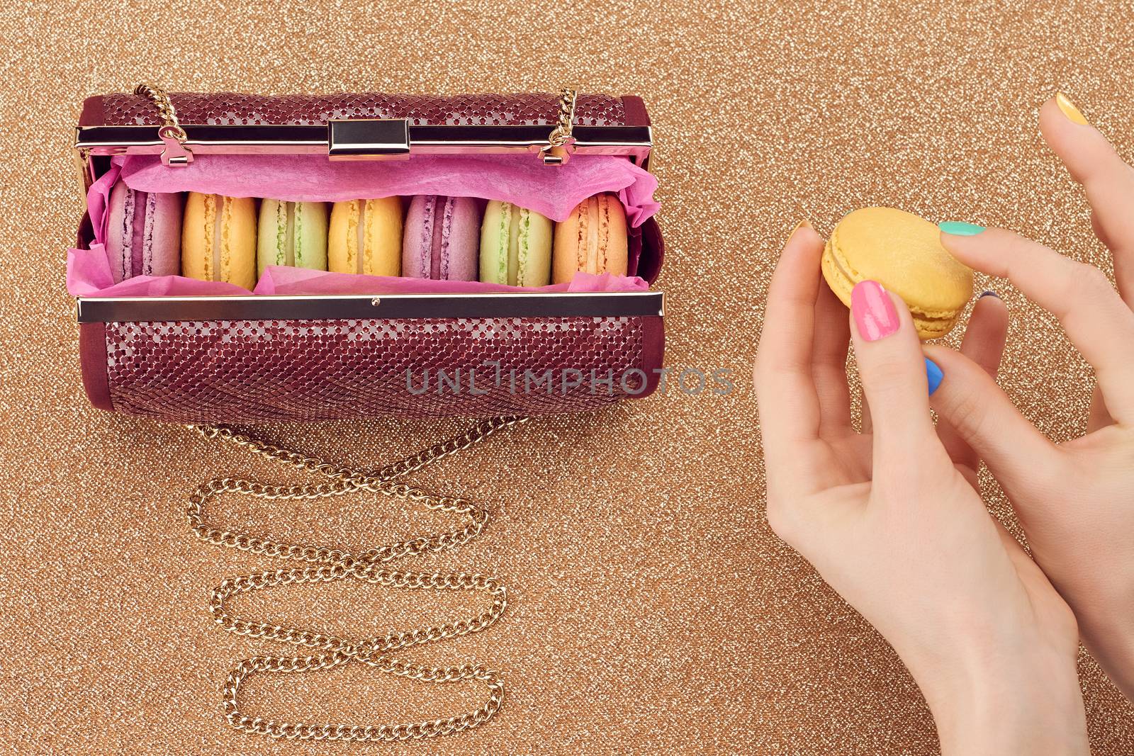 Macarons french in handbag, woman hands. Luxury shiny glamor fashion clutch. Sweet colorful dessert. Unusual creative art, gold party background, bokeh, copyspase. Vintage