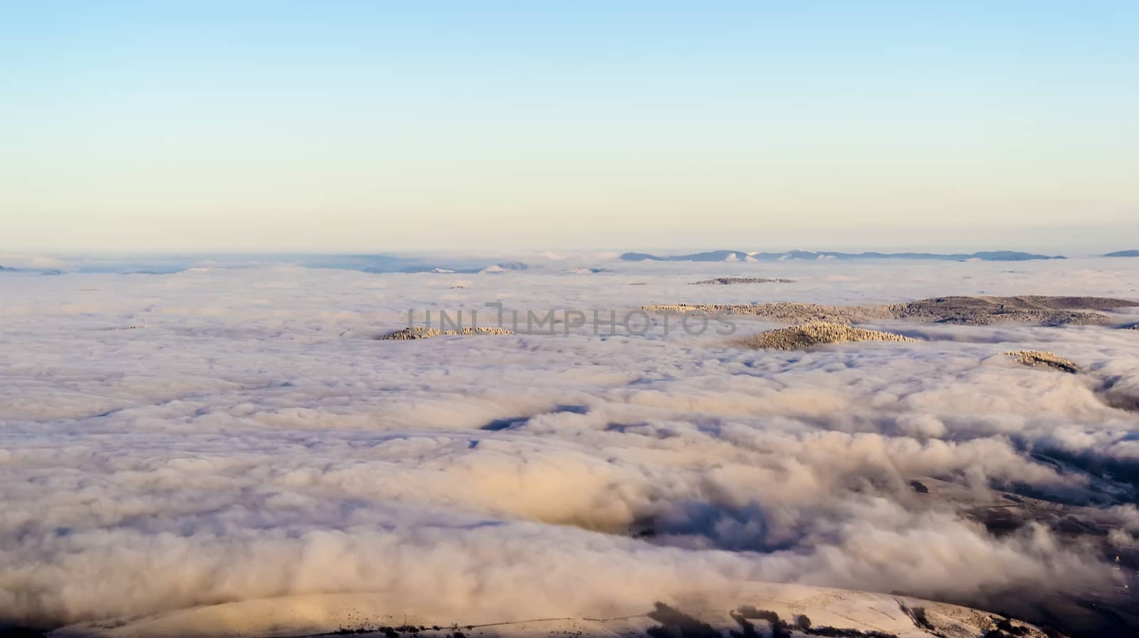 Scenic view, from the mountain top, of the clouds in the valleys. The sky is clear. Evening sunlight falling on the clouds. Some peaks are seen on the horizon. Winter. Carpathian Ukraine