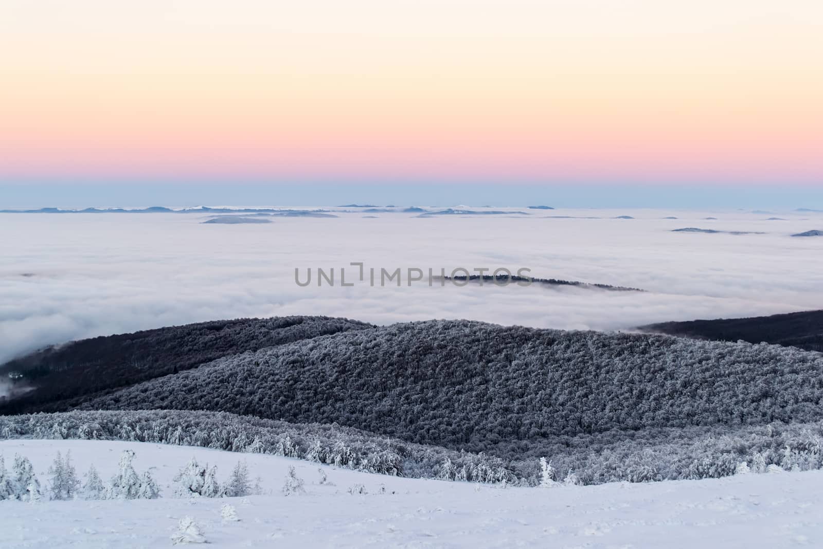 Scenic winter landscape above the clouds. The sky is clear. After dusk. Some mountains are seen on the horizon.