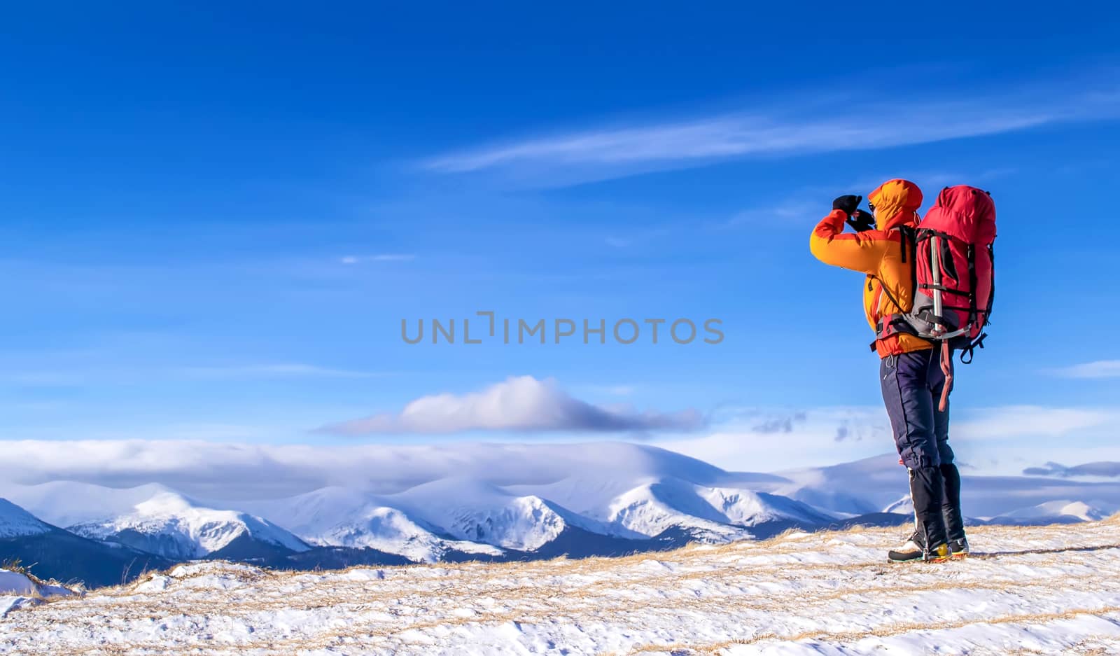 Tourist with a backpack takes a picture of mountain range in the background of the blue sky. Carpathian, Ukraine.