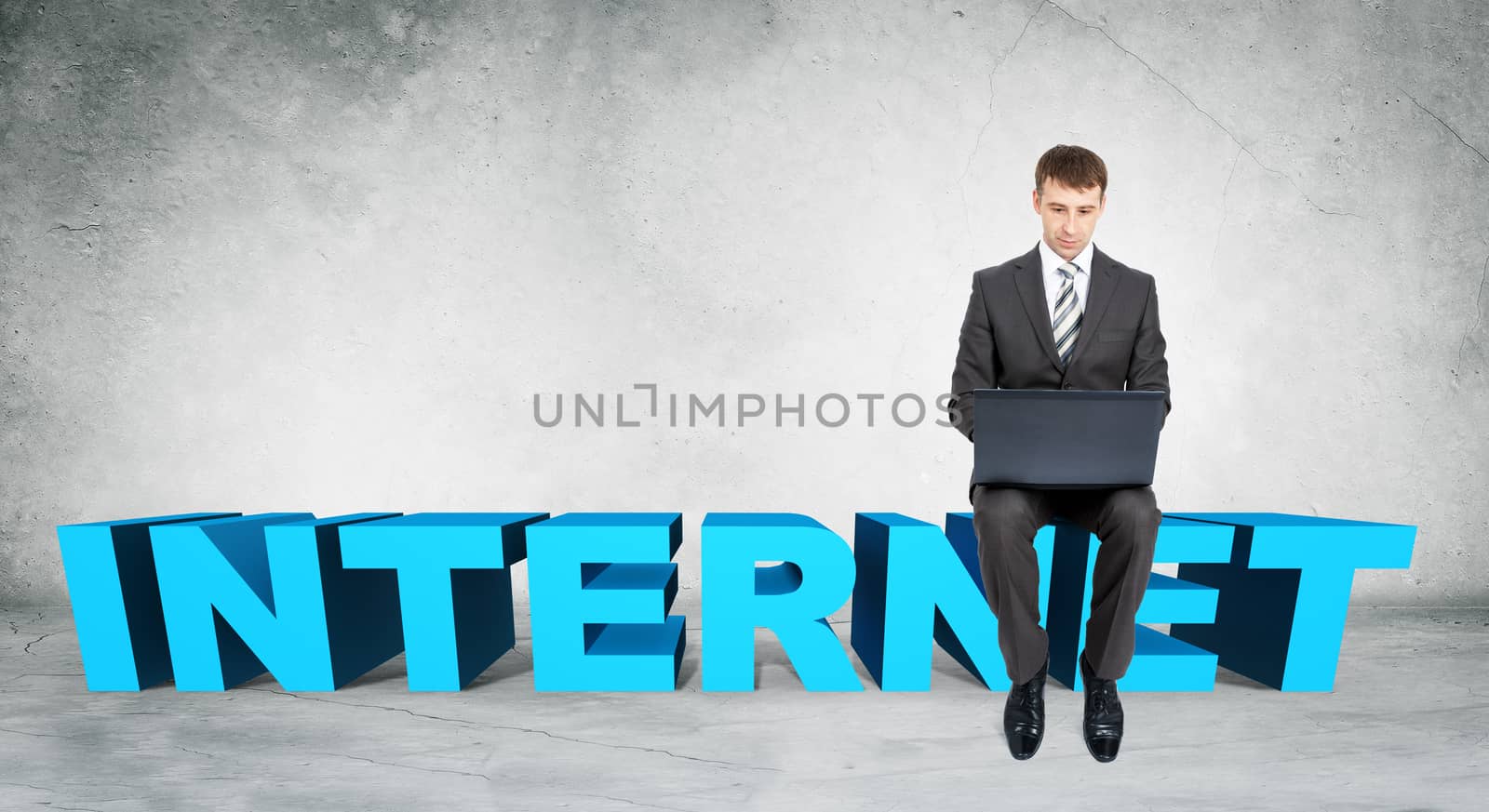 Businessman working on laptop and sitting on word internet on grey wall background