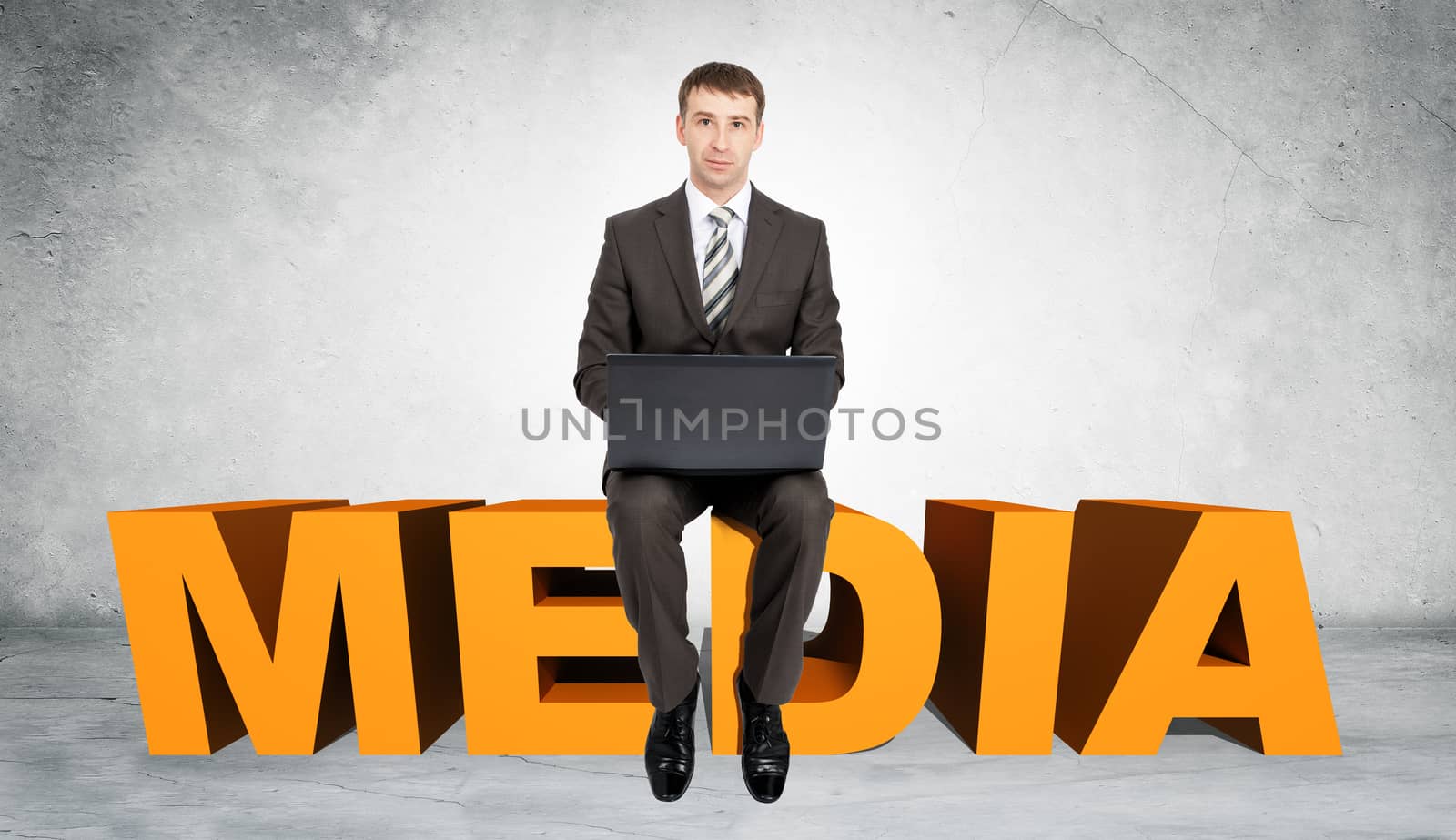 Businessman working on laptop and sitting on word media on grey wall background