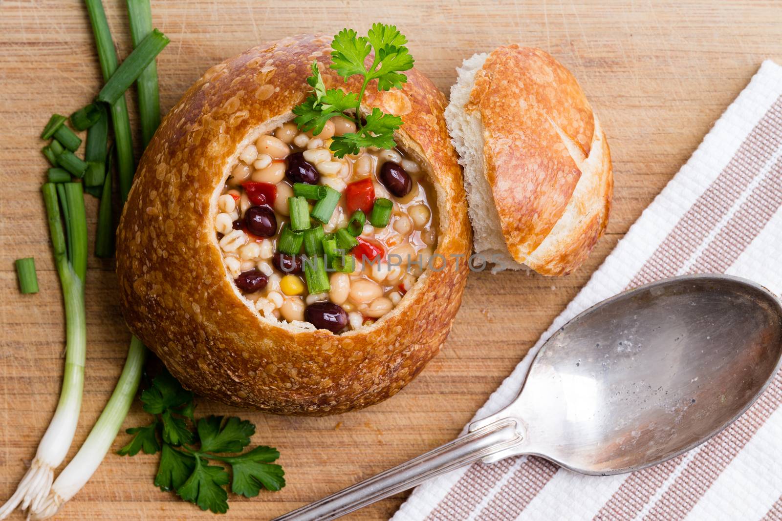 Top view of delicious bread bowl with beans, barley and vegetables next to pieces of green onion and cilantro and spoon