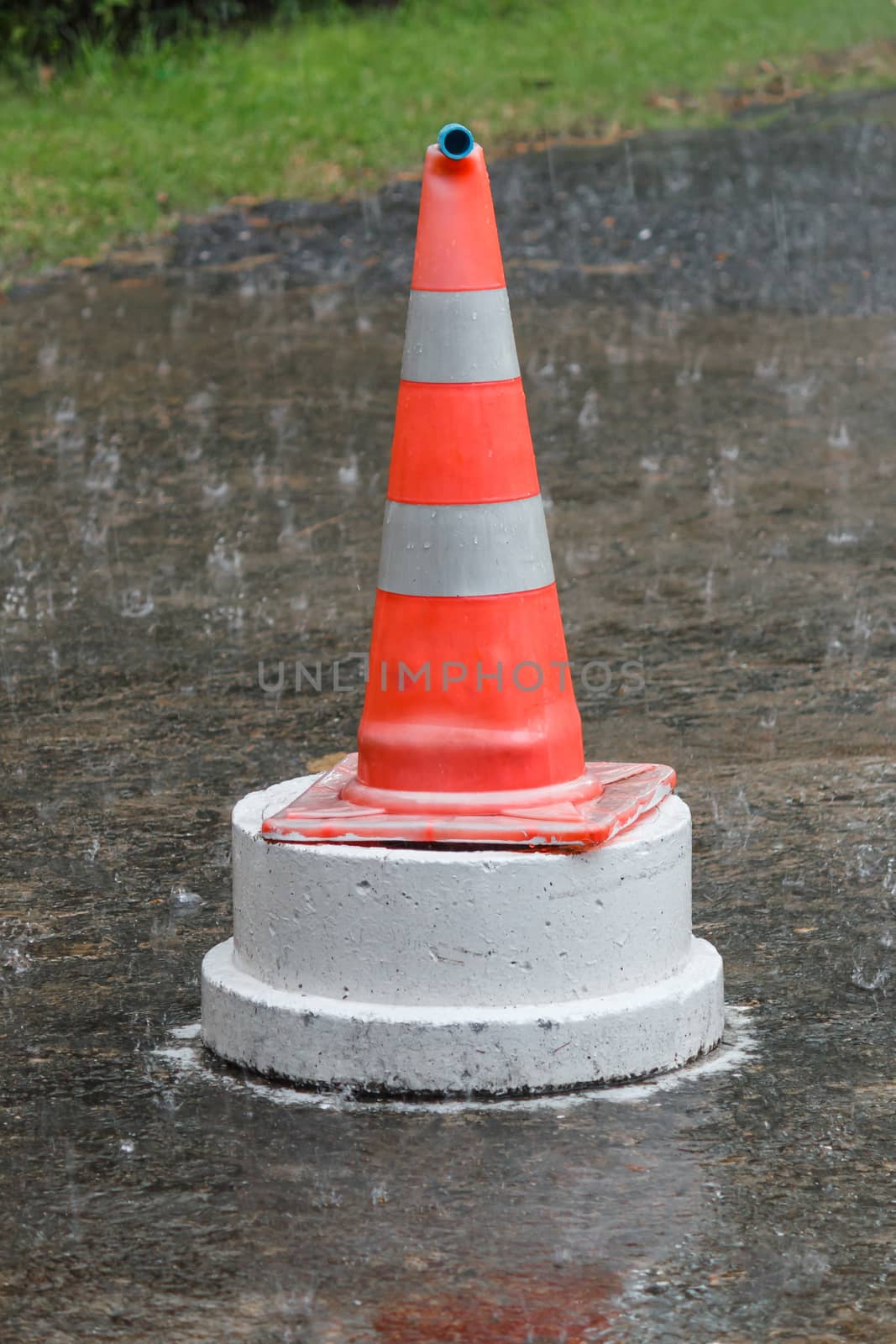 Traffic cone standing in the rain middle of the road.