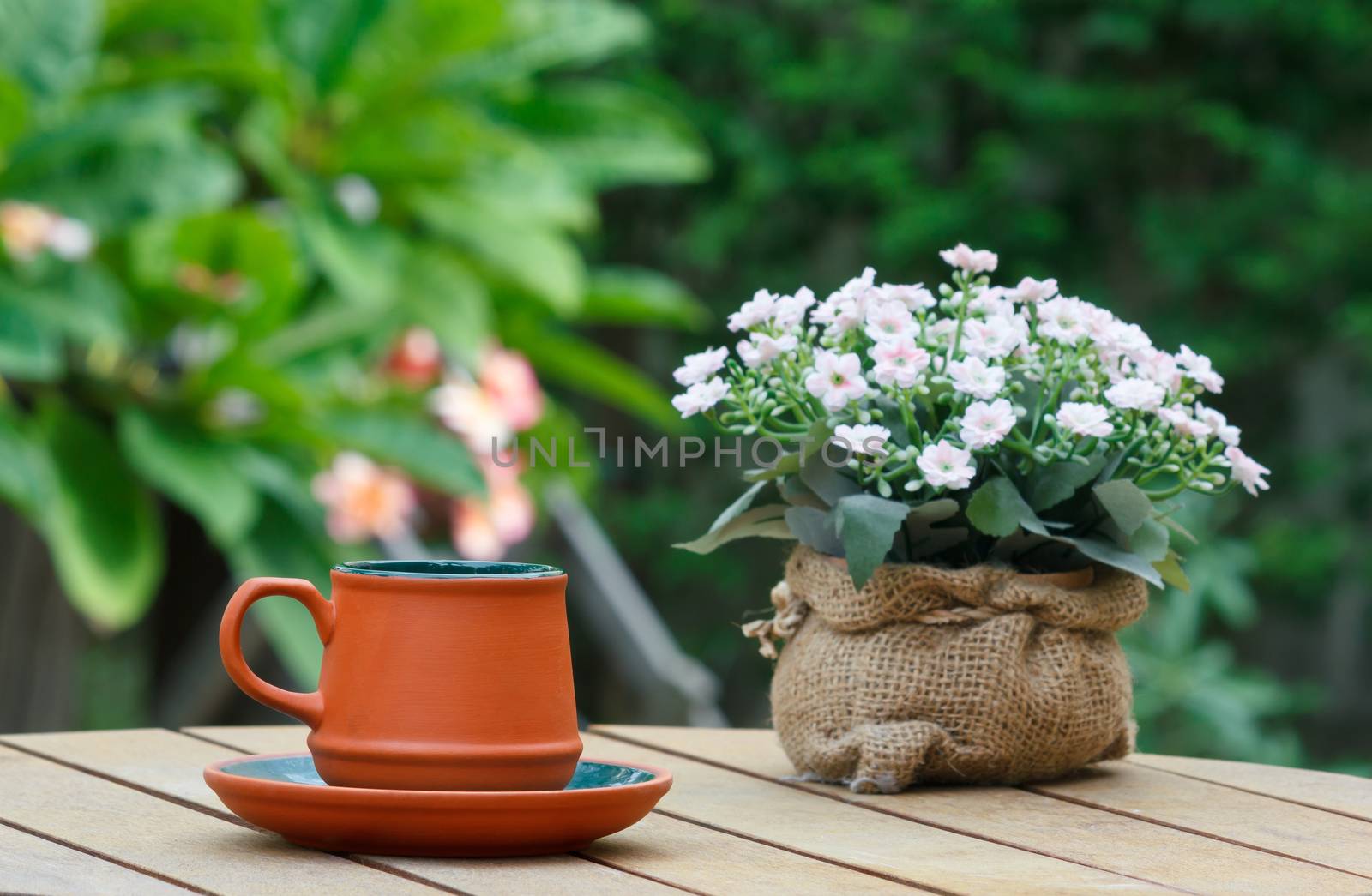 Cup of coffee and flowers on the wooden table with tree in background.Focus on the cup.