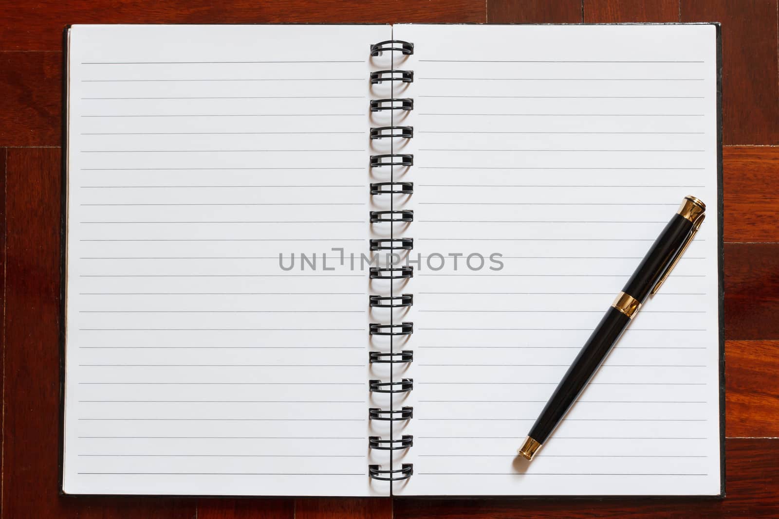 Notebook and pen. Blank white page. Wooden floor in the background.