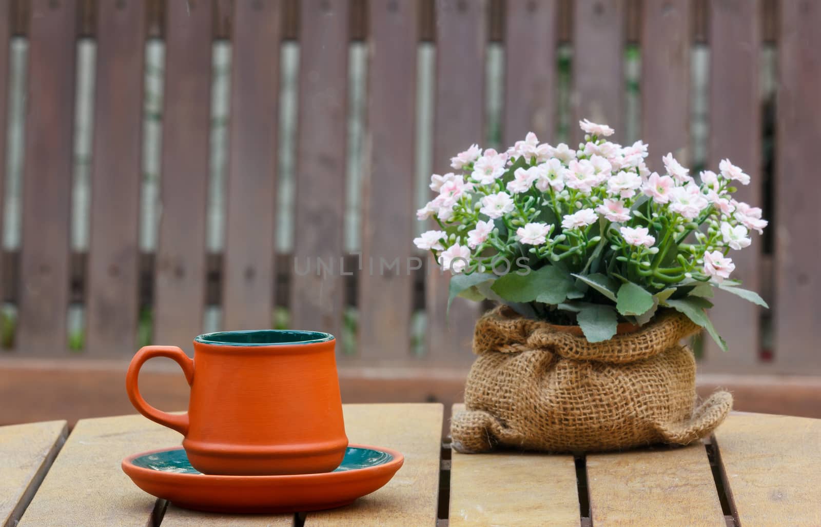 Cup of coffee and flowers on the wooden table with wooden seat in background.Focus on the cup.