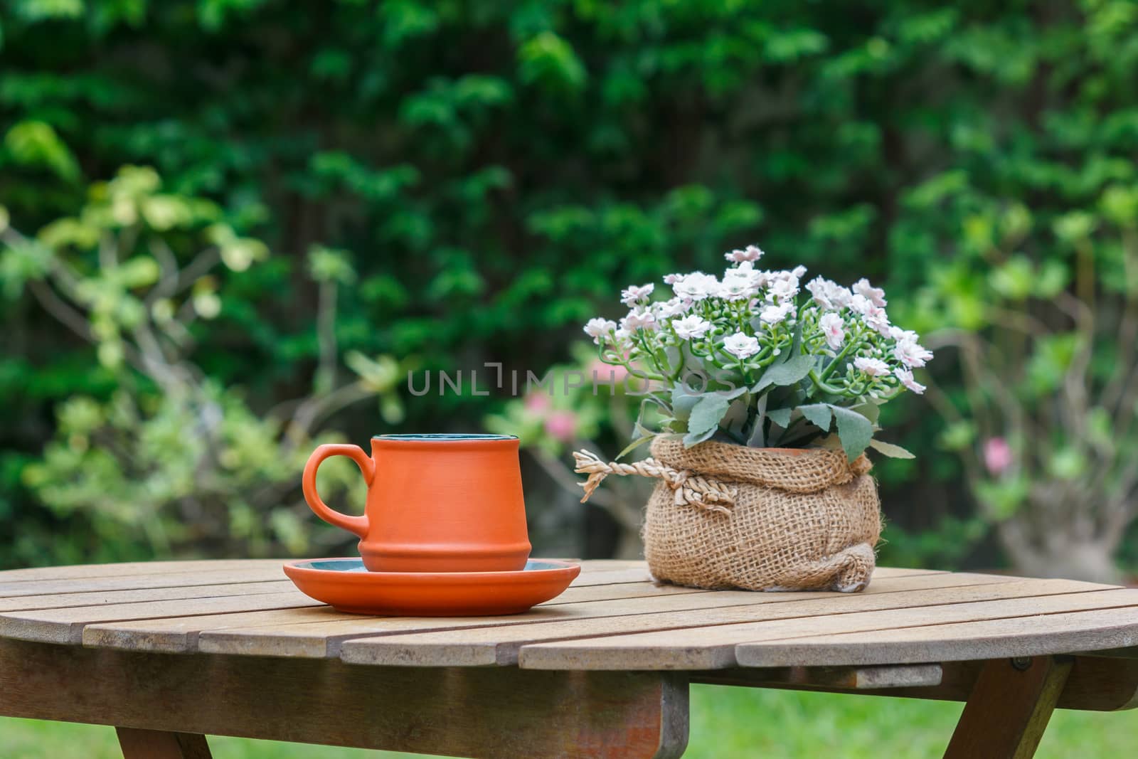 Cup of coffee and flowers on the wooden table with tree in background.Focus on the cup.