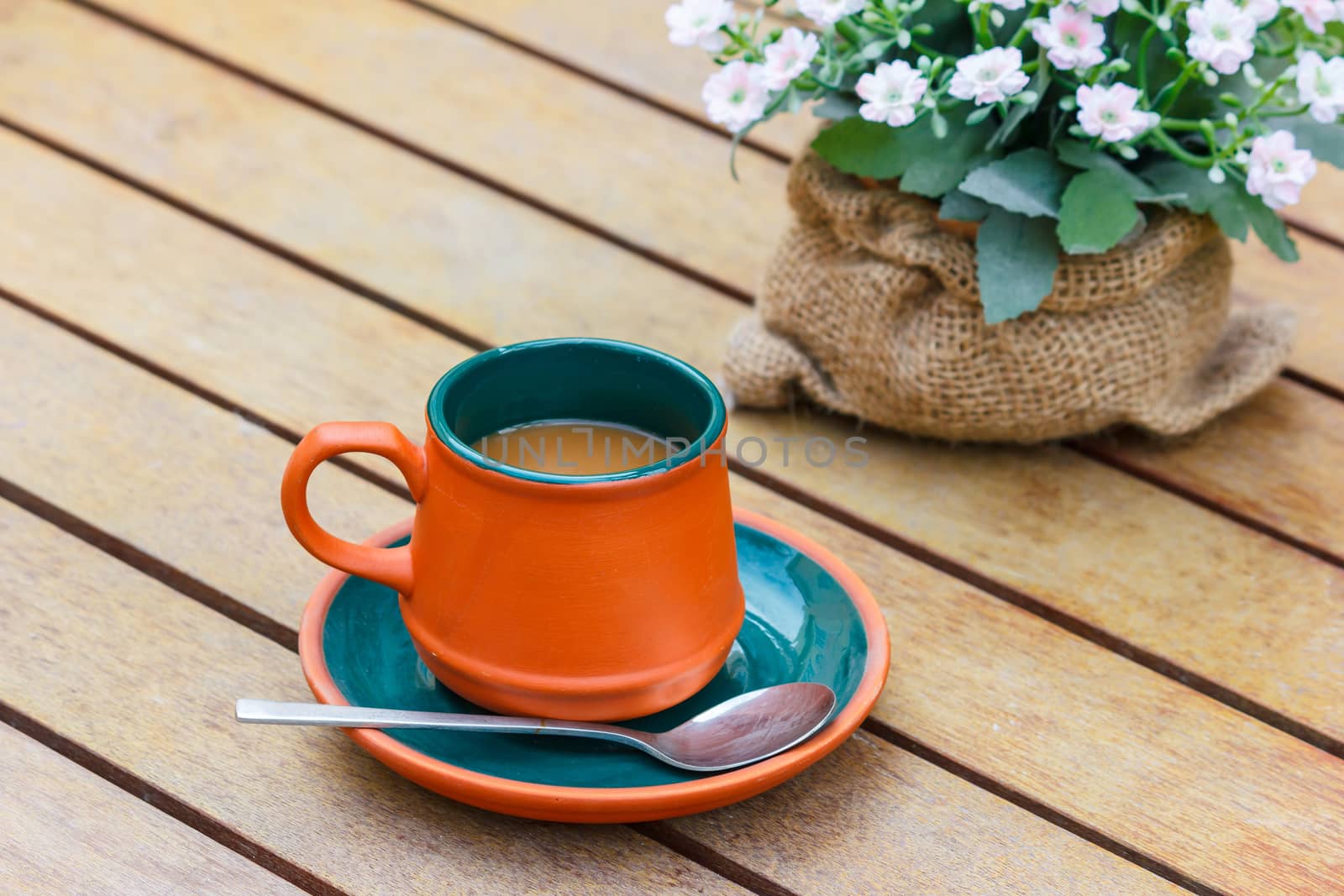 Hot coffee and flowers on the wooden table.Focus on the cup.