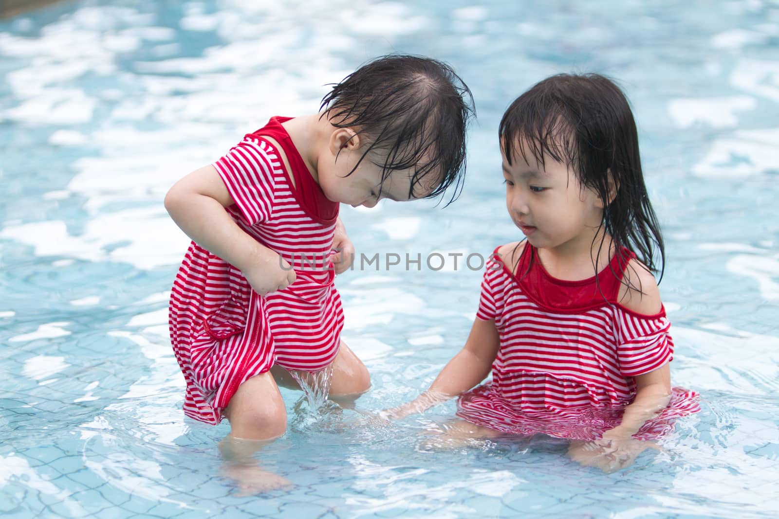 Two Little Sisters Playing in Water in Swimming Pool