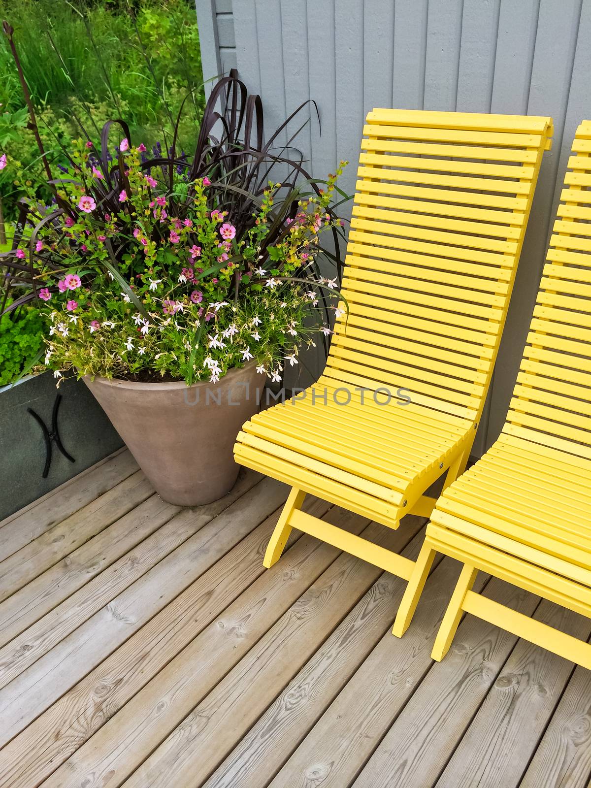 House exterior decorated with yellow chairs and big pot with flowers.