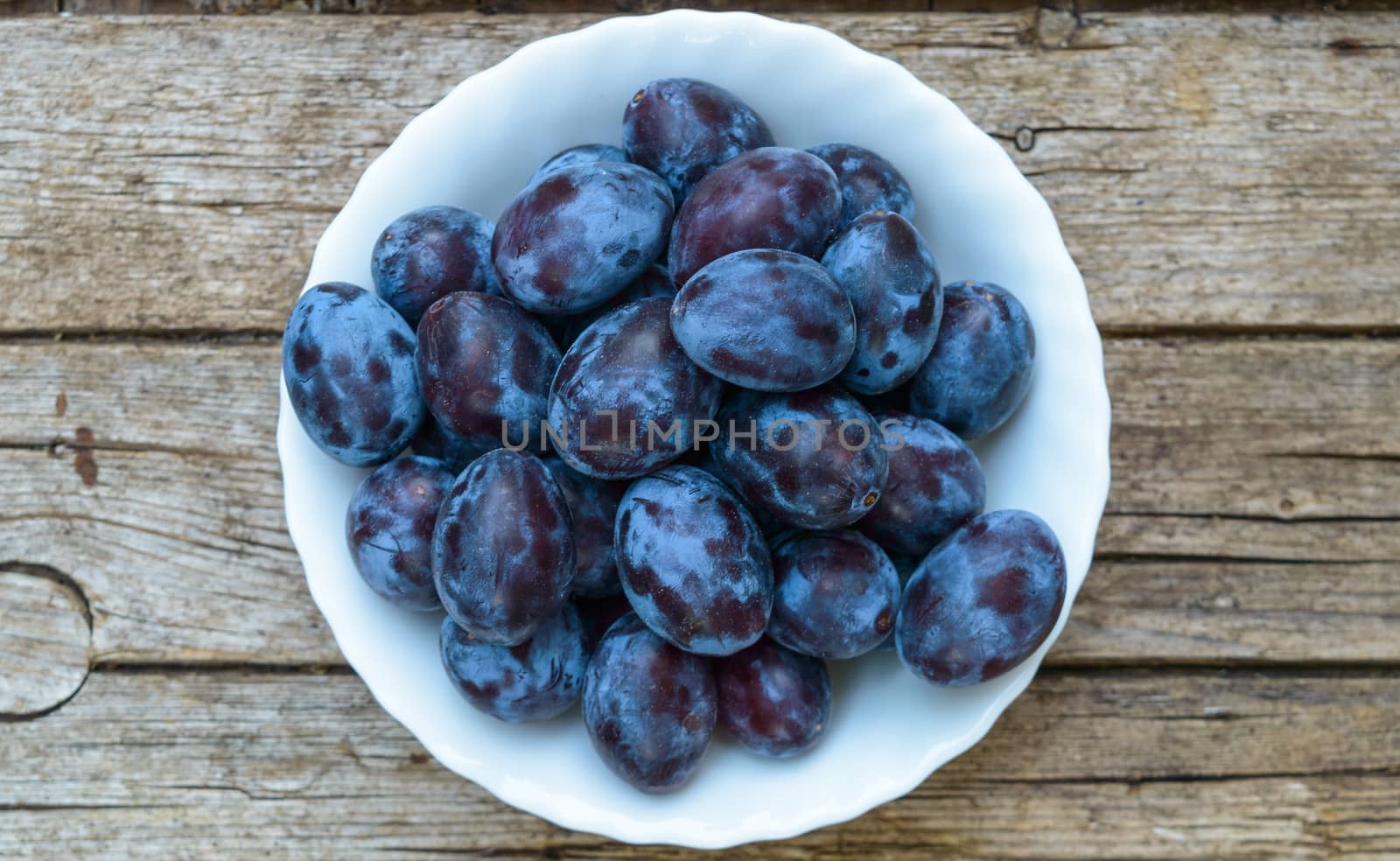 Plate full of fresh plums on a wooden background 