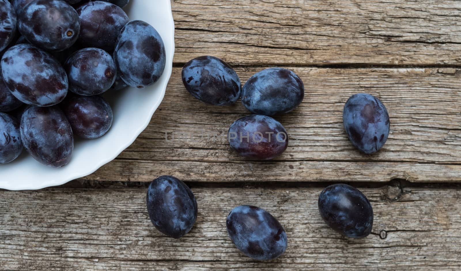 Plate full of fresh plums on a wooden background  by radzonimo