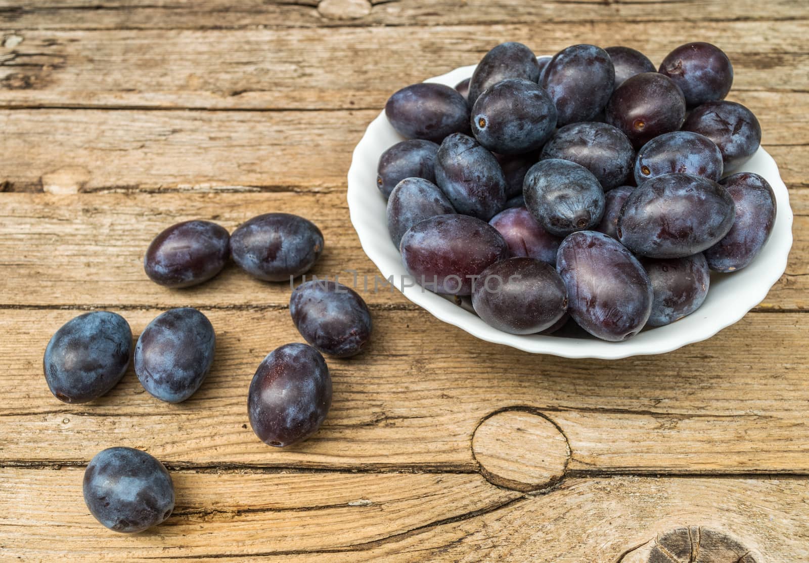 Plate full of fresh plums on a wooden background 