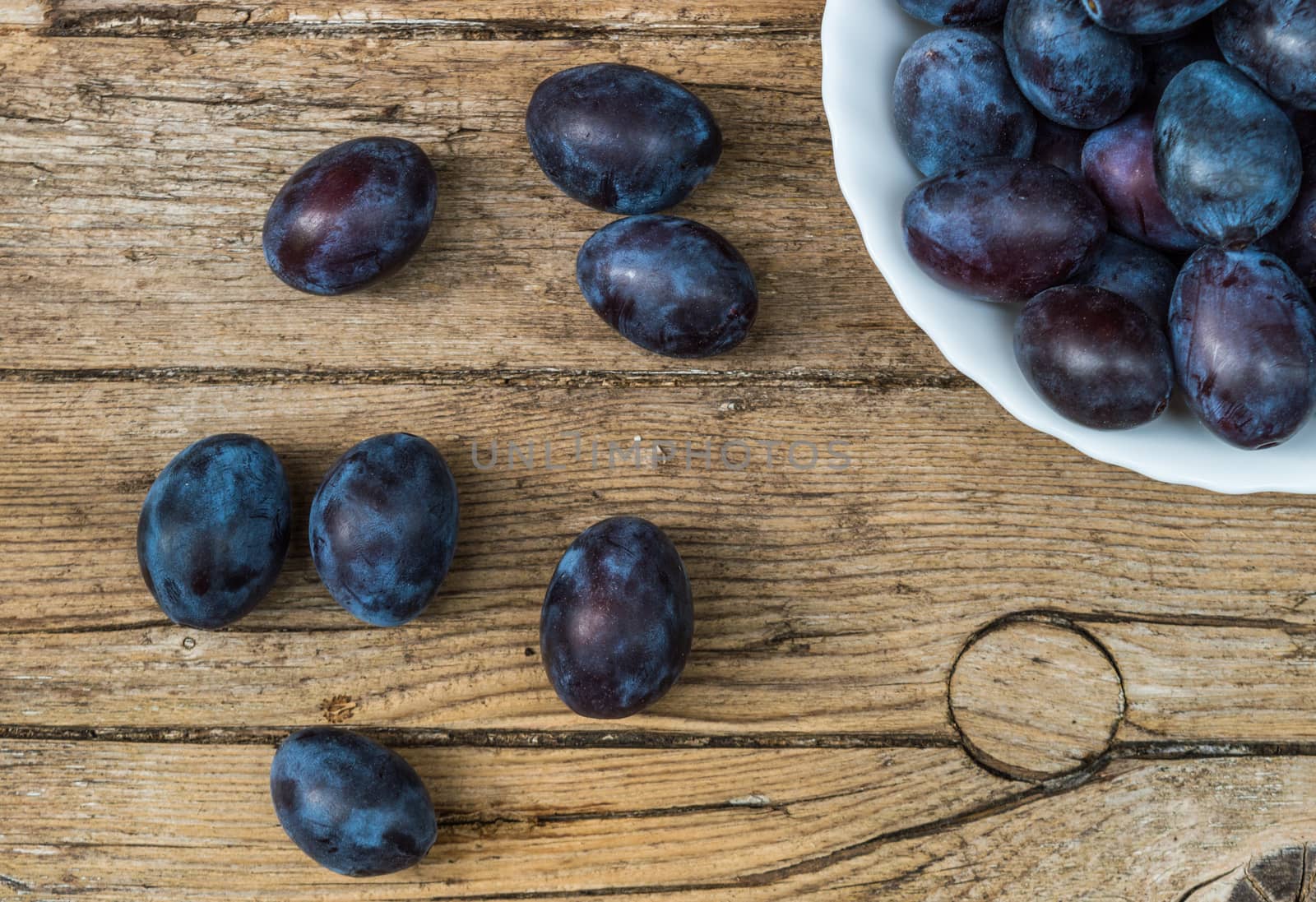 Plate full of fresh plums on a wooden background 