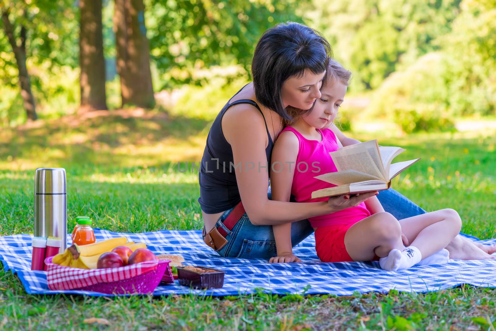 Mom and daughter reading a book on the lawn in the park by kosmsos111