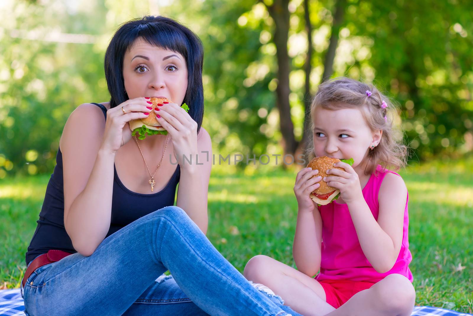 Mom and daughter eating tasty burgers on a picnic by kosmsos111