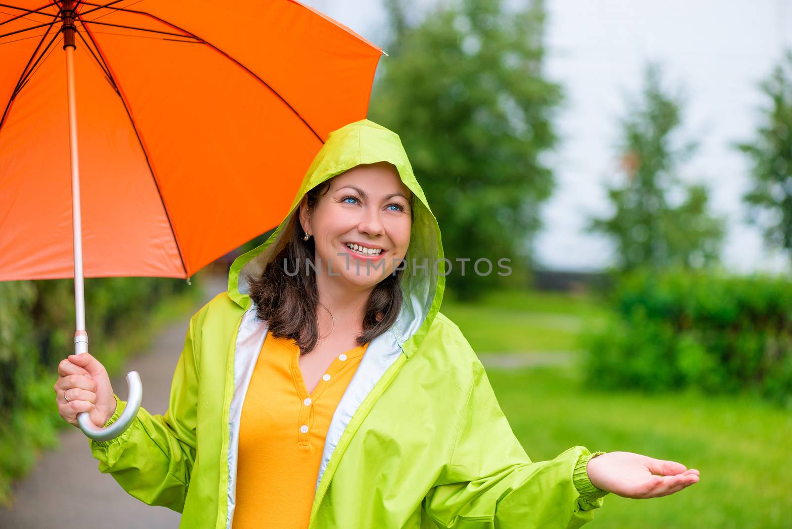 beautiful girl in a green raincoat and with an umbrella under the rain