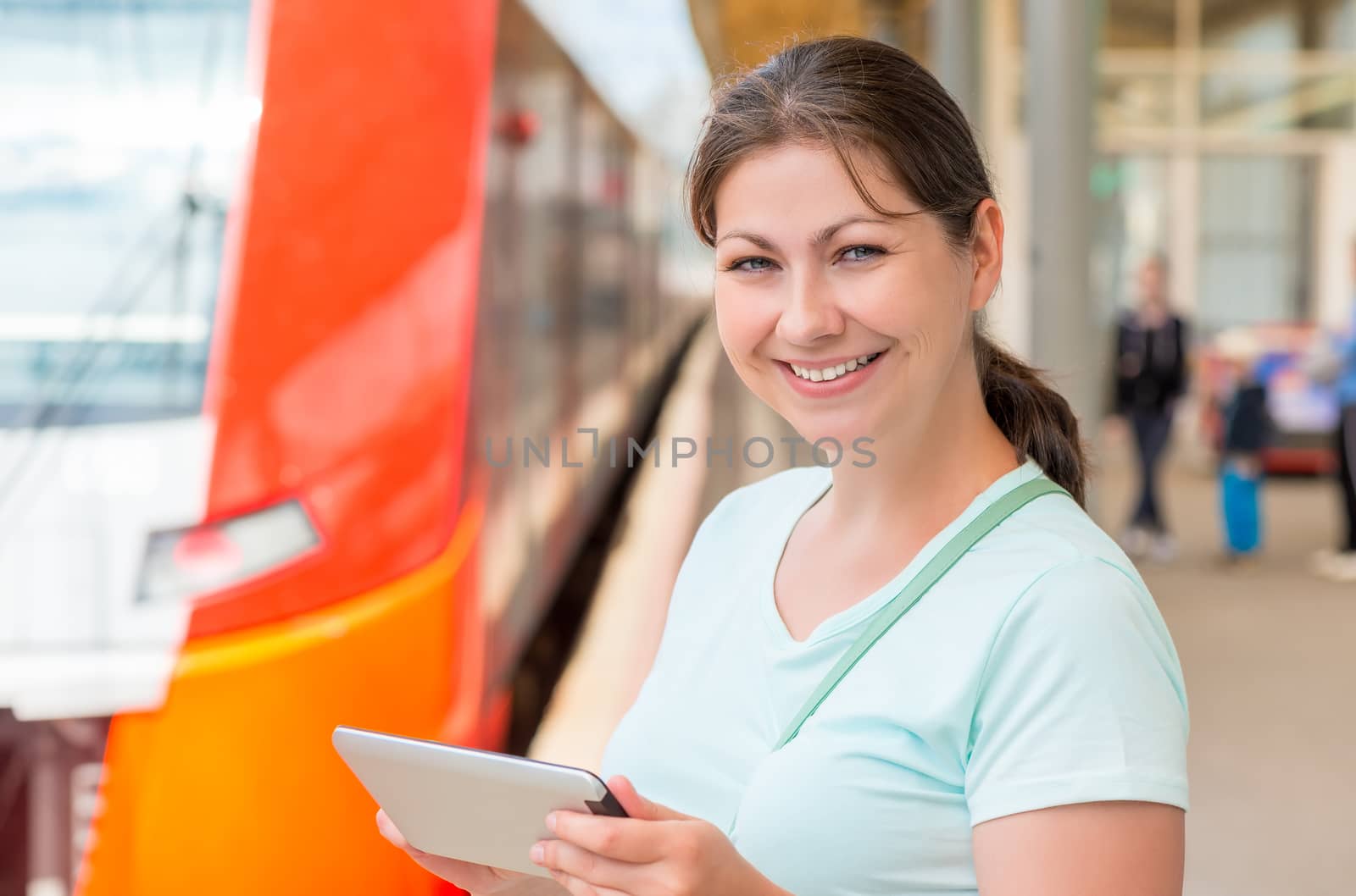 Brunette holding a tablet computer standing at the railway station