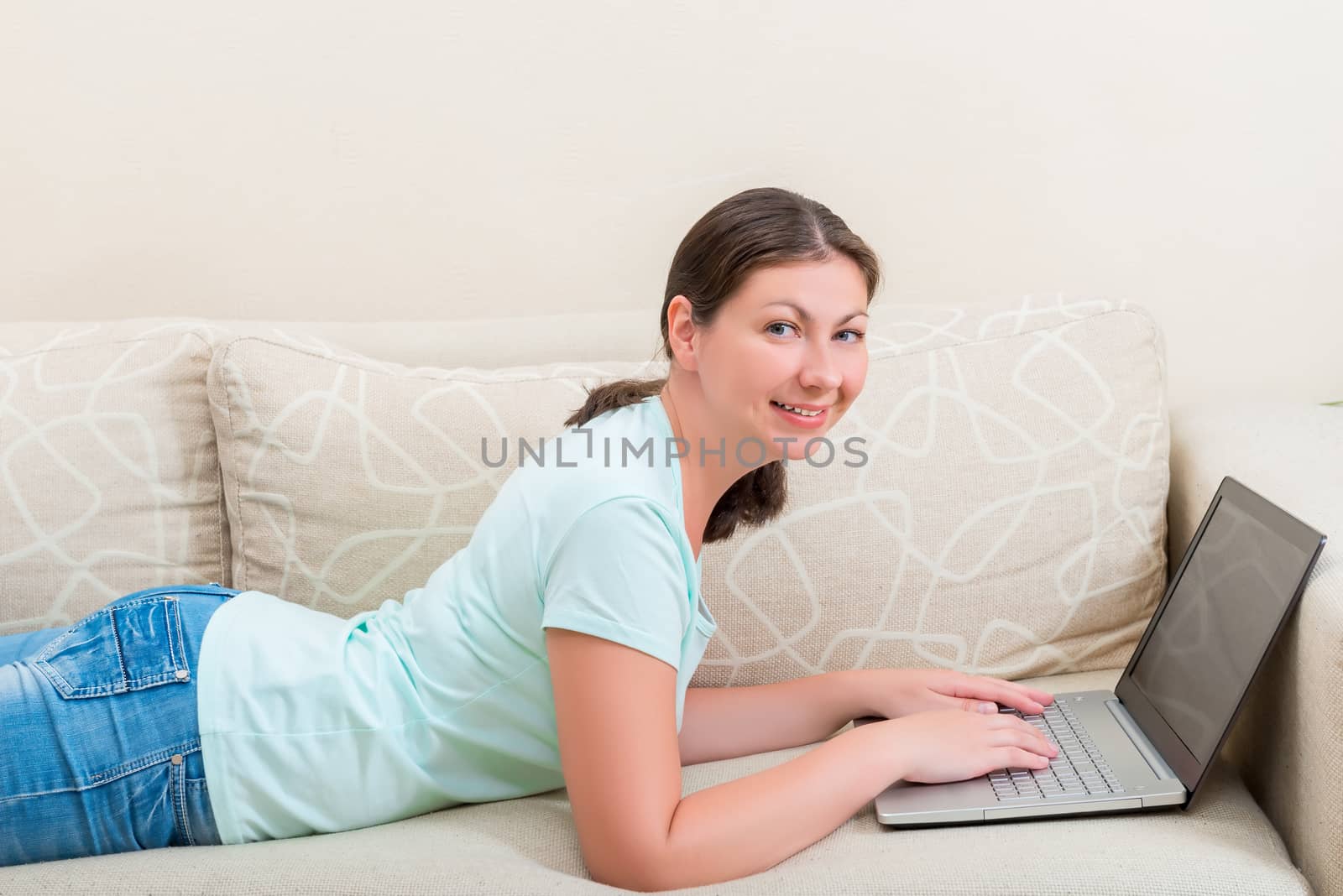 beautiful woman working on a laptop while lying on the couch