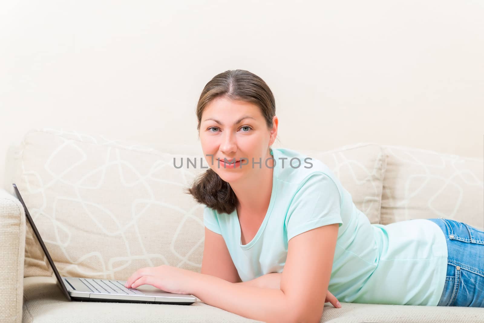 woman with laptop lying on the couch comfortably by kosmsos111