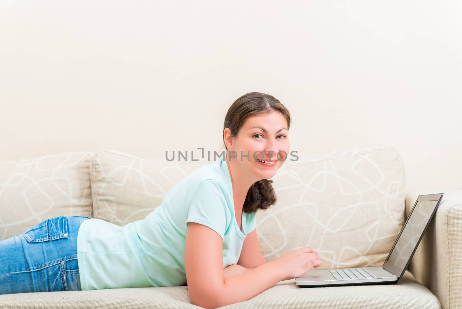 portrait of happy girl with a laptop lying on the sofa by kosmsos111