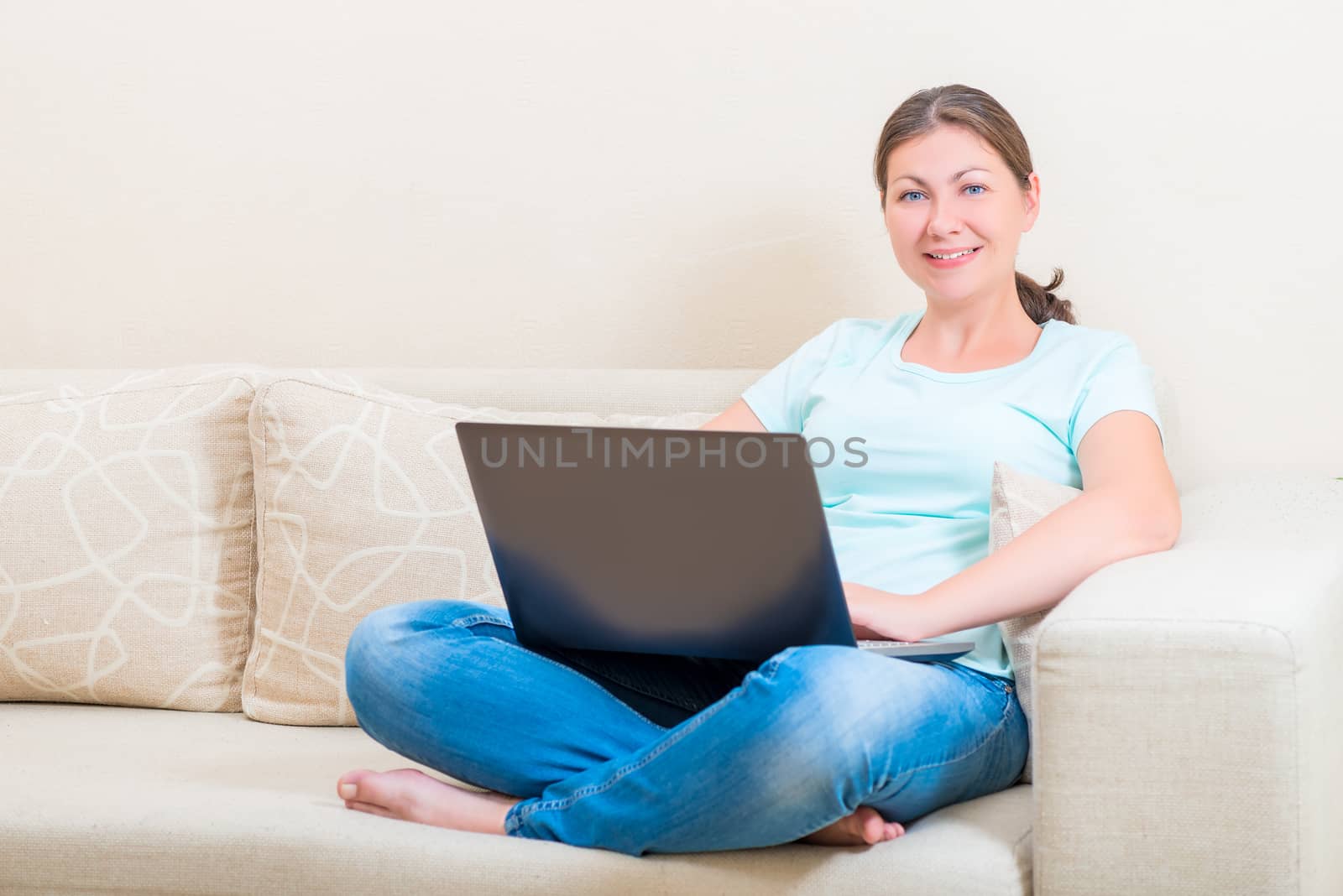 Beautiful girl smiling while sitting on a sofa with a laptop by kosmsos111