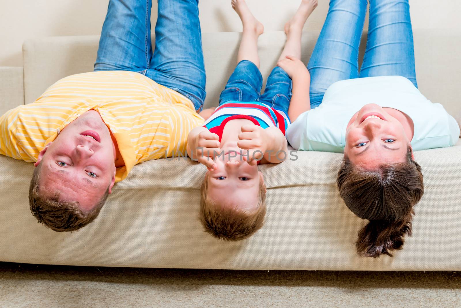 portrait of a happy family lying on couch head down by kosmsos111